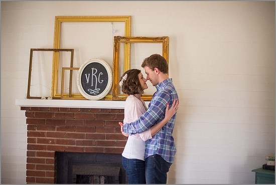 Couple embraces near fireplace with vintage decor and monogram
