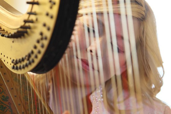 Blonde woman playing a harp with a focused expression on her face