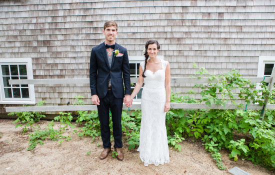 Newlyweds hold hands in front of a wood building, outdoor wedding