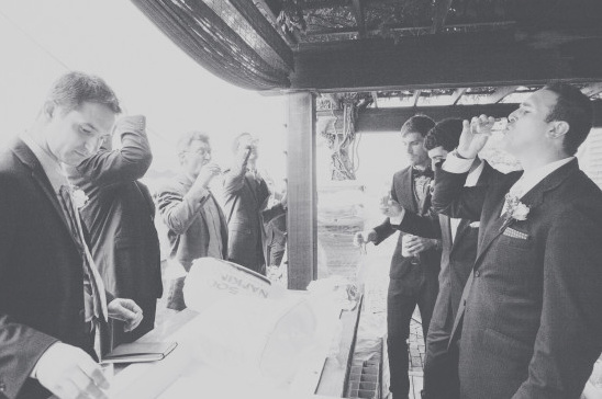 Men in suits raise a glass, celebrating under an outdoor canopy