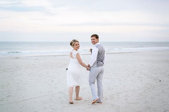 Newlyweds on the beach holding hands and looking back at camera