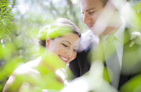 Joyful bride and groom embracing through vibrant green foliage in love