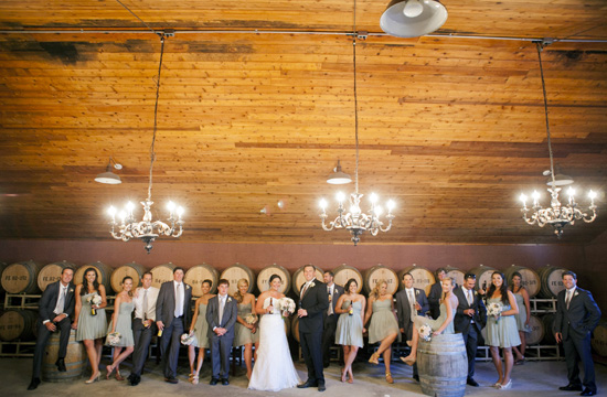Wedding party stands in front of wine barrels at the venue
