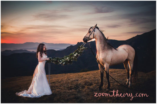 Bride and horse with floral garland against sunset mountains