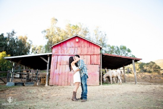 Couple kissing in front of a red barn, with horses nearby