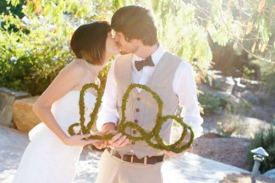Newlyweds share a kiss while holding a love sign outdoors