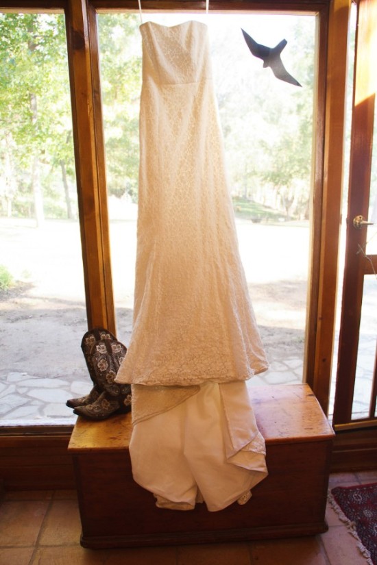 Elegant wedding dress hanging by window with cowboy boots