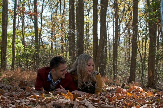 Couple laying in fall leaves in a vibrant autumn forest setting