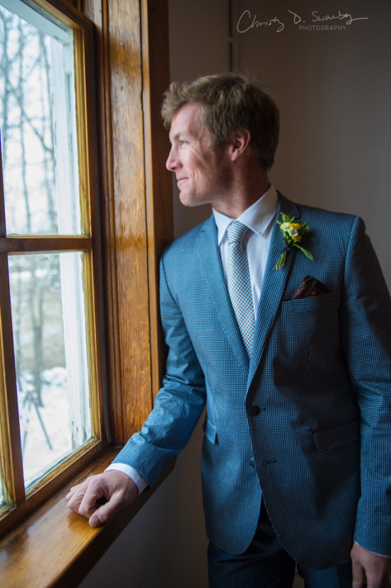 Groom in blue suit looks out the window on wedding day
