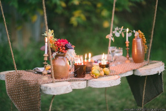 Rustic outdoor dinner setting on a swing table with candles and flowers