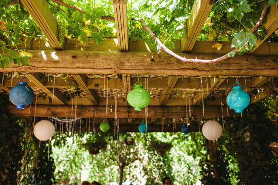 Festive paper lanterns adorn a wooden pergola in a garden