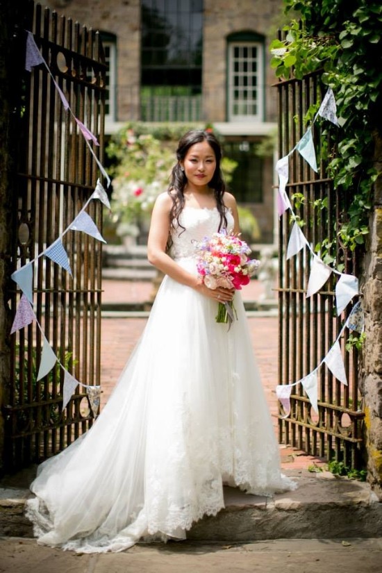Bride in a white dress holding flowers, posing in front of a gate