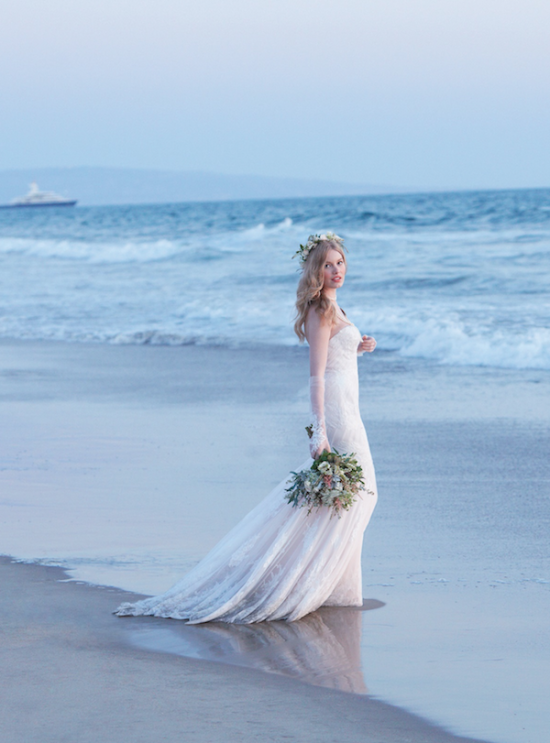 Elegant bride in white dress with bouquet on the beach shore