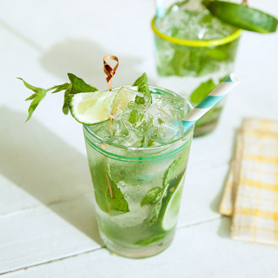 Refreshing Mojito cocktail with mint, lime, and ice cubes on a white table