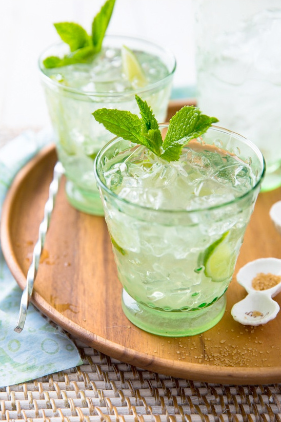 Refreshing mojitos garnished with mint and lime on a wooden tray