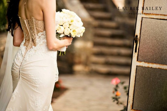 Bride from behind in lace corset dress holding white roses