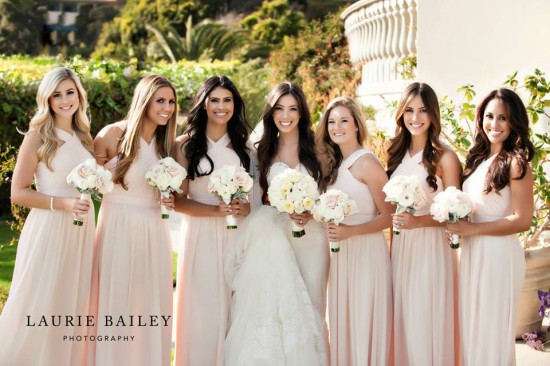 Smiling bride with bridesmaids in pale pink gowns outdoors