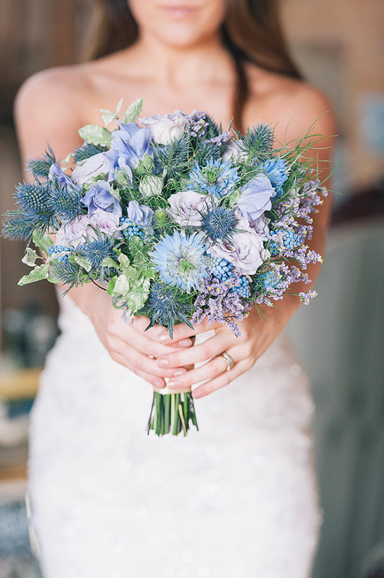 Bride holds blue and purple thistle wedding bouquet