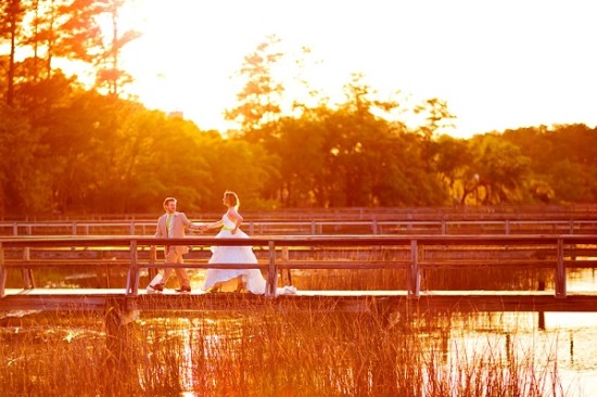 Bride and groom stroll over sunsetlit wooden bridge