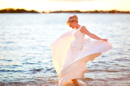 Joyful bride twirls white dress by sea at golden hour