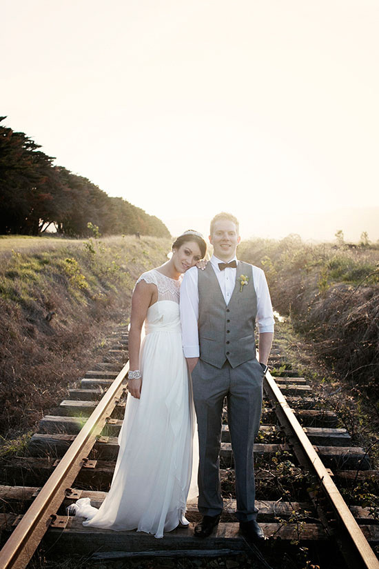 Bride and groom pose on railway track at sunset