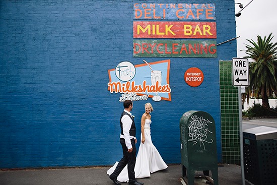 Bride and groom walk past vintage diner sign on blue wall