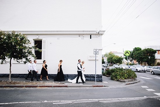 Wedding party walks sidewalk by white building street view
