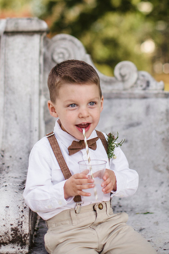 Young boy in bow tie drinking from a straw outdoors