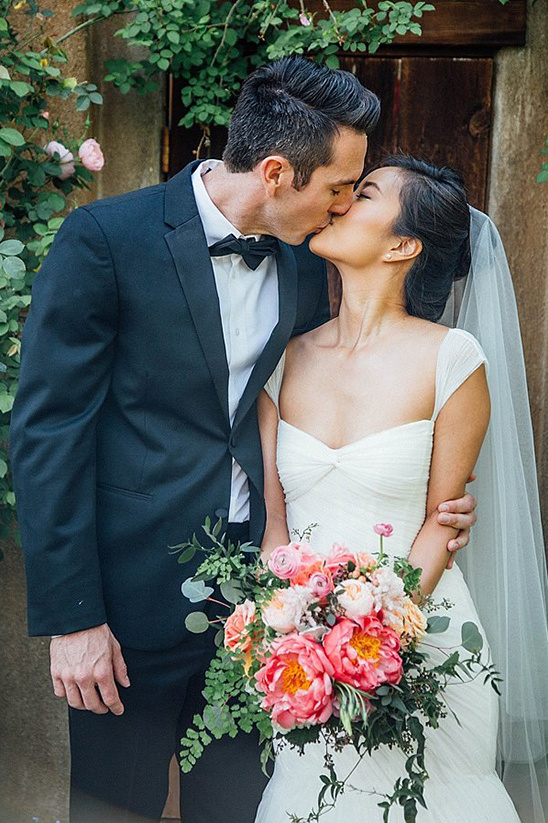 Newlyweds share a kiss with floral bouquet at their wedding