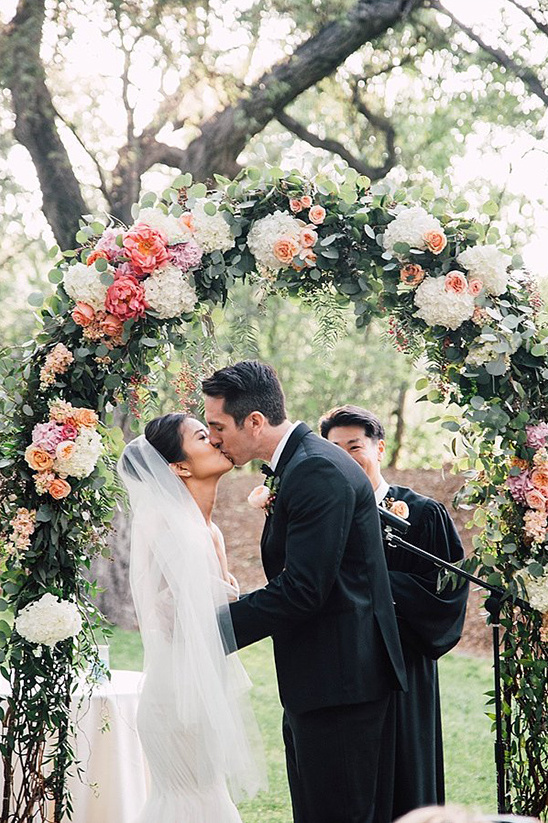 Bride and groom kiss under floral wedding archway