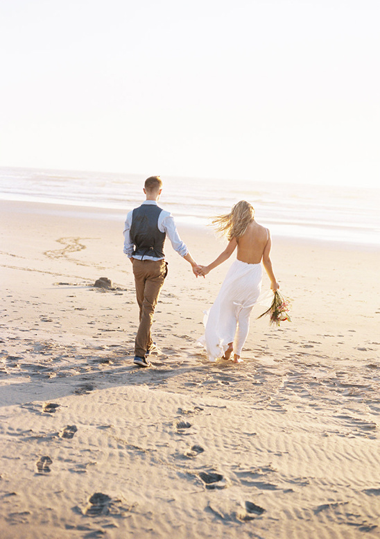 Newlyweds holding hands walking along the beach at sunset