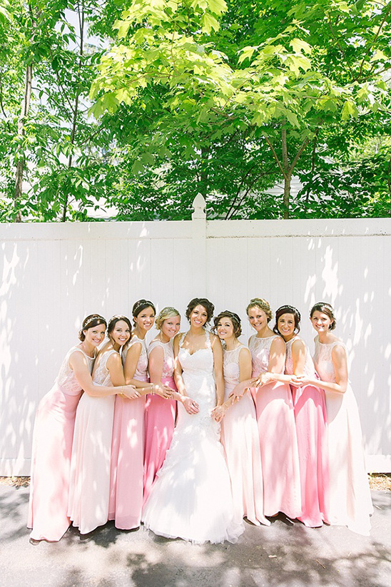Bride with bridesmaids in pink dresses by white fence