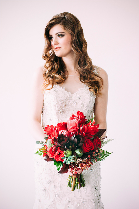 Bride in white lace dress holding a red floral bouquet