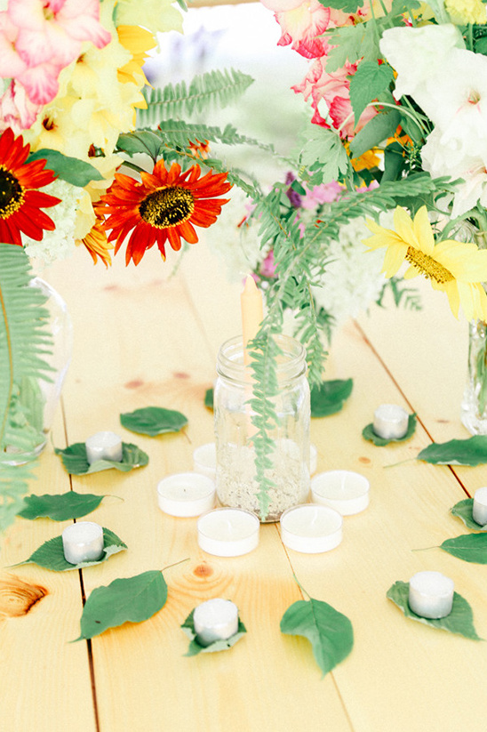 Floral centerpiece with candles and leaves on wood table