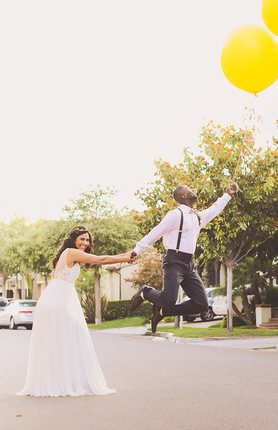 Happy bride and groom joyfully jumping with yellow balloons