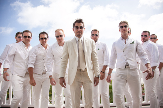 Groom and groomsmen in white suits with sunglasses smiling