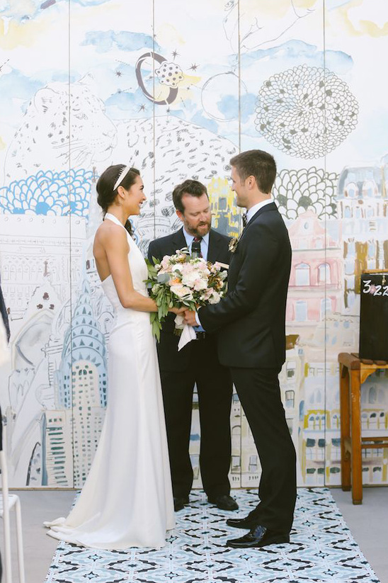 Bride and groom exchanging vows before whimsical city backdrop