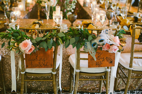 Wedding chairs decorated with greenery, masks, and signs reading My dashing husband and My darling wife