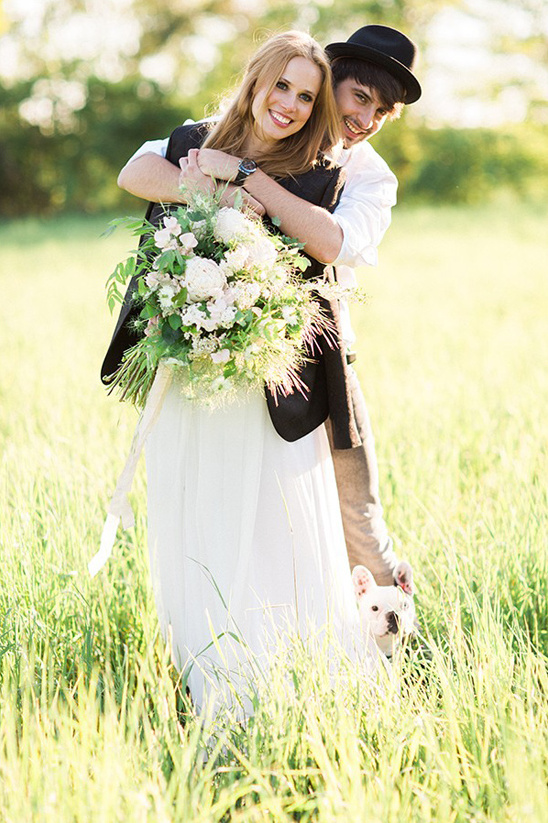 Happy couple embracing in field with dog and bouquet