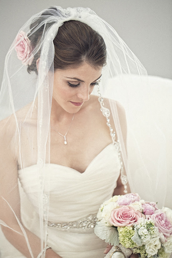 Elegant bride in white dress, veil and bouquet of pink roses