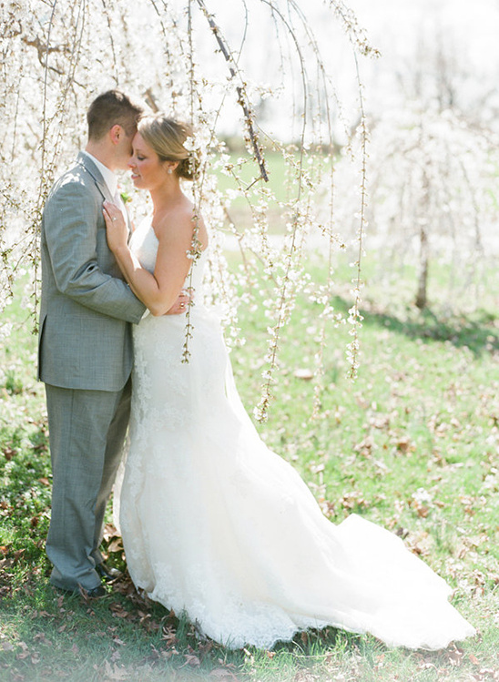 Romantic wedding couple embrace under blossoming tree in sunlight