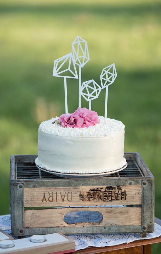 Wedding cake with geometric toppers and pink flowers on a crate