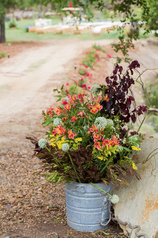 Vibrant floral arrangement in a metal bucket by a garden path