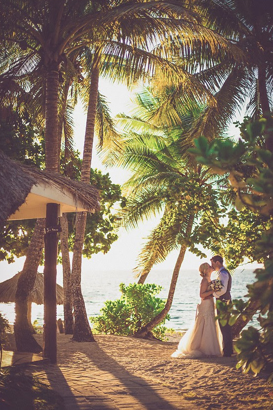 Romantic beach wedding couple kissing under palm trees