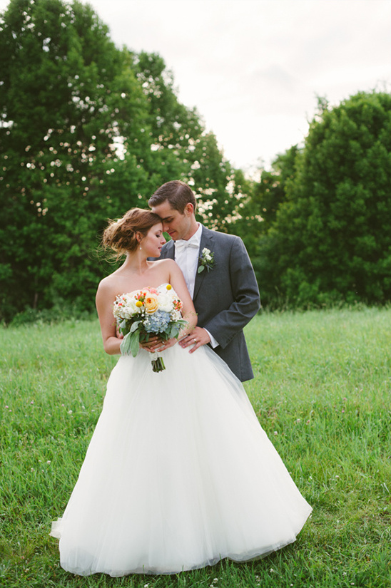 Wedding couple embracing in a meadow with lush greenery and a bouquet