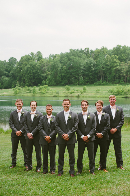 Groomsmen in gray suits pose by a lake for a wedding photo