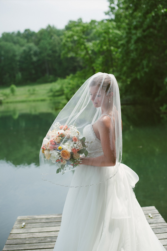 Bride in white dress holding flowers on a wooden pier near a lake