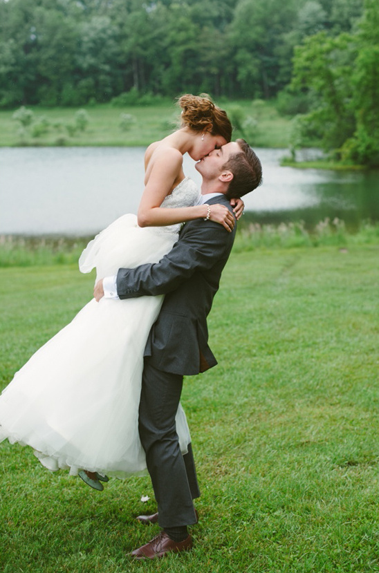 Groom lifts bride and kisses, wedding day joy by the lake