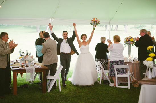 Newlyweds celebrating as they walk into their wedding reception, happy guests clapping