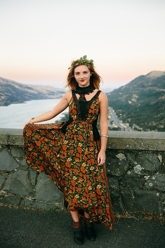 Woman in floral dress with wreath poses by scenic overlook